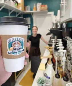 close up of to-go coffee cup with a smiling woman in the background